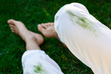 Barefoot girl sitting dirty stain of grass on white pants on a background of green field. top view. outodors