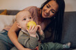 © Zamrznuti tonovi - Baby boy sitting on the couch with his mom and eating an apple