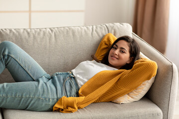 Wall Mural - Total relax. Happy arab woman lying with hands behind head on comfortable sofa and smiling, having great day off