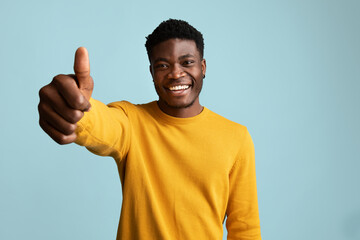 Wall Mural - Cute black guy showing thumb up, posing on blue