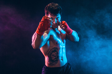 Portrait of muscular kickbox or muay thai fighter who punching on smoke background. Sport concept.