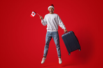 Man Wearing Santa Hat Jumping In Air With Canadian Flag And Suitcase