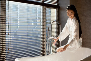 Wall Mural - Happy attractive chinese lady sitting on bath, copy space