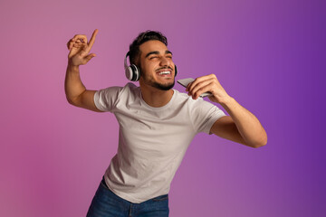 Poster - Young Arab man in headphones singing song, using smartphone as mic, enjoying new mobile music app in neon light