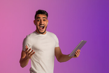 Poster - Shocked millennial Arab guy in earphones holding tablet pc, screaming wow, cannot believe his luck in neon light