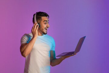 Poster - Online victory, big sale, shocking offer. Excited young Arab man in headphones looking at laptop computer in neon light