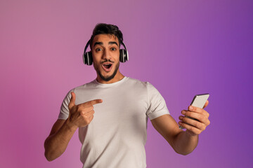 Poster - Surprised young Arab guy in headphones pointing at smartphone, shocked over online sale in neon light