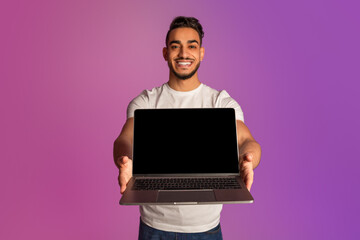 Poster - Happy millennial Arab man holding laptop with black blank screen, showing free space for your mockup in neon light