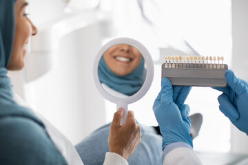 Wall Mural - Restorative Dentistry. Muslim Female Patient Holding Mirror And Looking At Her Smile