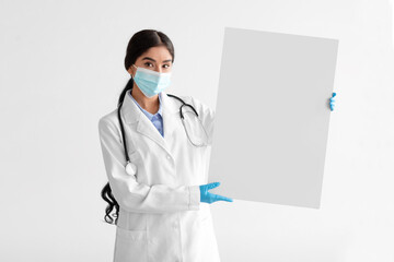 Wall Mural - Serious millennial indian woman therapist in white coat with stethoscope in protective mask, gloves hold banner