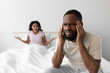 Upset angry young african american wife yelling at sad unhappy husband on white bed in bedroom interior