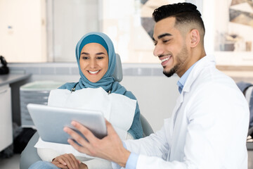 Wall Mural - Dentist With Digital Tablet Showing Teeth Treatment Plan To Muslim Female Patient