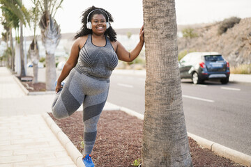 Wall Mural - Curvy african woman stretching during workout routine outdoor at city park - Focus on face