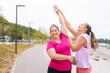 © dikushin - Medium shot of cheerful fitness female trainer have personal training with positive overweight young woman outdoor in summer morning. Instructor help fat woman lose weight outside.