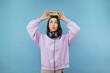© bodnarphoto - Pretty student girl in headphones and pink sweatshirt puts books on her head and looks up with funny face, isolated on blue background