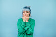© bodnarphoto - Cute teen girl in a green sweatshirt and colored hair stands on a blue background and looks at the camera with a slight smile on his face.