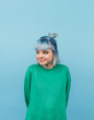 © bodnarphoto - Cheerful teen girl with blue hair and in a green sweatshirt looks aside with a smile, isola on a blue background.vertical
