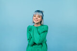 Fototapeta Uliczki - Portrait of a beautiful girl with blue hair with a smile on her face isolated on a blue background, looking at the camera.