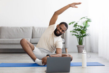 Happy young black bearded athlete man in white clothes do stretching or exercises for hands on mat