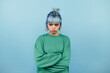 © bodnarphoto - Portrait of a displeased teen girl with long hair standing on a blue background and looking away.