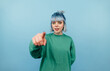 © bodnarphoto - Positive teen girl with blue hair points a finger at the camera and smiles on a blue background