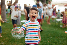 Emotional Child With Soap Bubbles. An Emotional Boy With A Big Bubble. Summer Weekend, Recreation, Children's Animation In The Park In The Fresh Air, Animation Program With Soap Bubbles.