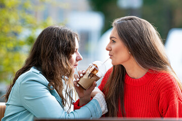 two milenial girlfriend spend free time in outdoor cafe with cocktails, laughing and talking