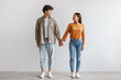 © Prostock-studio - Full length of millennial Asian couple smiling and looking at each other, holding hands, standing against white wall