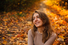 Beautiful Girl Is Sitting On Yellow Leaves In The Park. Attractive Woman Wearing Beige Sweater And Black Pants Is Walking In Autumn Park. Bright, Warm Sunny Autumn Day With Yellow Background.
