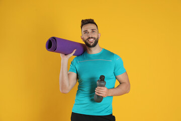 Wall Mural - Handsome man with yoga mat and bottle of water on yellow background