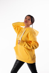 Wall Mural - Attractive woman of Latin appearance wears a yellow hoodie on a white background. The girl looks sexy and happy. The elegant brunette is wearing a bright sweatshirt. All-season clothing