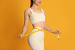 © New Africa - Happy woman in sportswear measuring waist with tape on yellow background, closeup