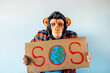 © karrastock - Man with monkey mask showing a sign that says S.O.S.