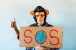 © karrastock - Man with monkey mask showing a sign that says S.O.S.