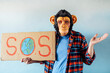 © karrastock - Man with monkey mask showing a sign that says S.O.S.