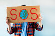 © karrastock - Man with monkey mask showing a sign that says S.O.S.