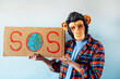 © karrastock - Man with monkey mask showing a sign that says S.O.S.