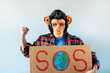 © karrastock - Man with monkey mask showing a sign that says S.O.S.