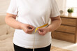 Overweight woman measuring waist with tape at home, closeup
