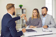 © Studio Romantic - Family buys real estate. Male real estate agent at meeting in office hands over keys to his new home to joyful young married couple. Concept of buying house or obtaining mortgage agreement.