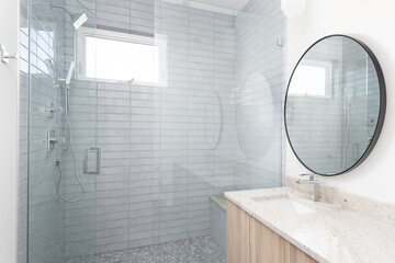 Wall Mural - A beautiful bathroom with a circular mirror, natural wood vanity cabinet, and grey tiled shower.