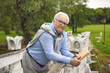 © Studio Romantic - Portrait of a positive smiling senior man walking in a summer park with a book in his hands. Chubby grandfather enjoys free time in retirement. Concept of serene old age.