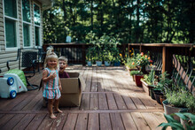 Small Girl And Boy Playing In A Box On Porch With Plants