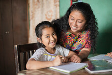 Hispanic Mom Helping Her Little Daughter Do Her Homework - Mom Teaching Her Daughter To Read And Write At Home - Mayan Family At Home