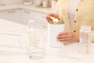 Woman preparing infant formula at table indoors, closeup. Baby milk