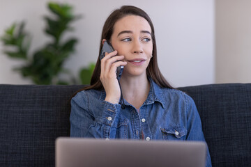 Poster - Caucasian woman at home using laptop computer sitting on a couch talking on cell phone