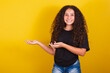 Brazilian, latin american girl for afro hair, yellow background, smiling, suggesting, suggestion, indication pointing with hands to the side, negative space for advertising and publicity,