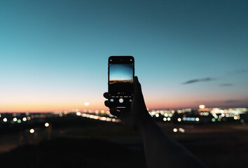 Person taking photo of a friend on mobile phone at sunset overlooking the city airport