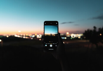 Person taking photo of a friend on mobile phone at sunset overlooking the city airport