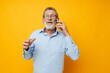 © Tatiana - Portrait elderly man gray beard with glasses talking on the phone yellow background